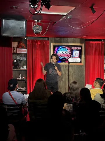 A seated audience watching a comedian beneath the All Good Comedy screen