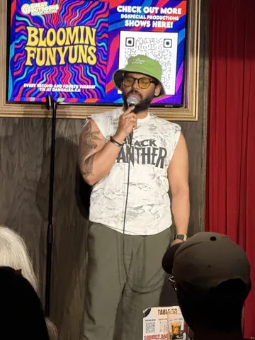 A comedian wearing a cap and a sleeveless shirt on the Bloomin Funyuns stage