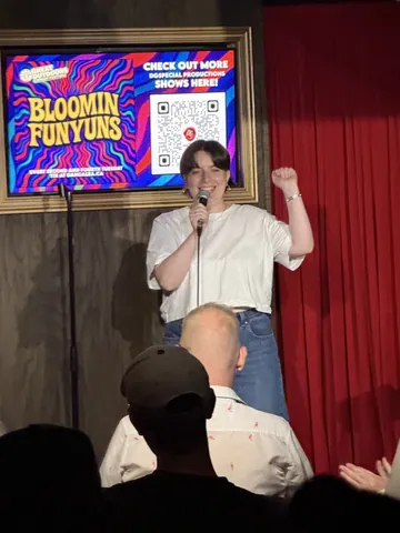 A comedian in a white top raising a fist while holding a microphone