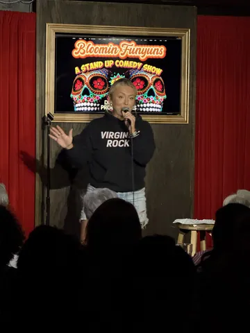 A comedian in a black T-shirt gesturing to the seated audience