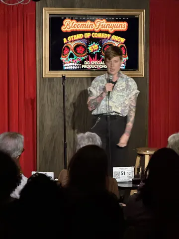 A comedian in a patterned shirt holding a microphone on stage