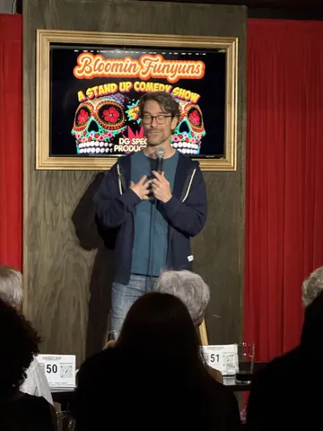A comedian in a navy sweater speaking into a microphone