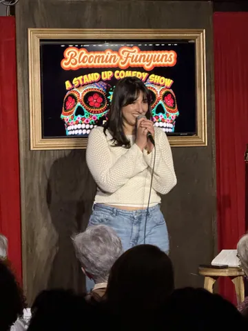 A comedian in a cream sweater performing in front of a Bloomin Funyuns screen