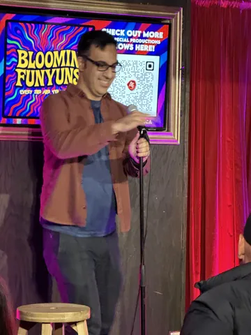A comedian in a colour-block shirt gesturing to the audience