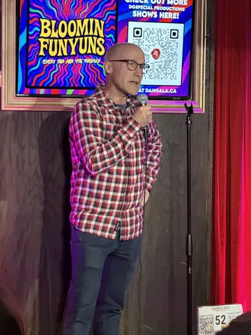 A comedian in a red checked shirt holding a microphone