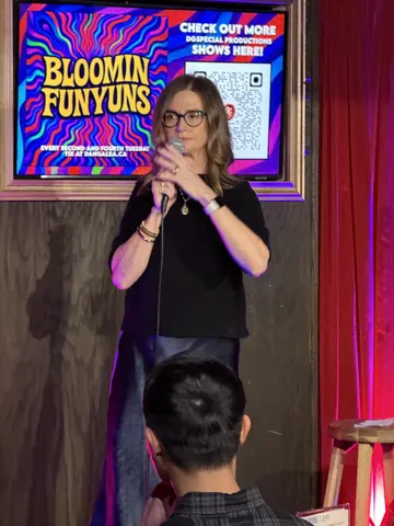 A comedian wearing glasses and a black top on the Bloomin Funyuns stage