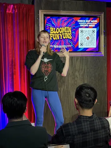 A comedian in a green graphic T-shirt gesturing beside the red curtains