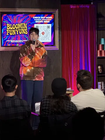 A comedian in a colourful orange and black shirt addressing the audience