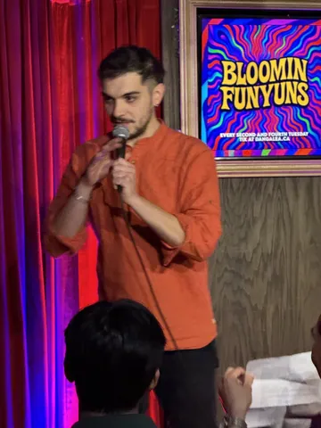 A comedian in an orange shirt speaking into a microphone