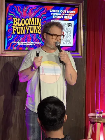 A comedian wearing glasses and a pale striped shirt performing on stage