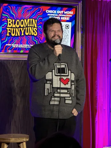 A comedian in a robot-print sweatshirt performing under purple lights