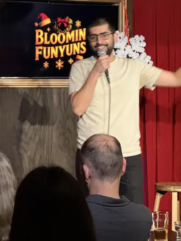 A comedian in a cream shirt extending an arm towards the audience