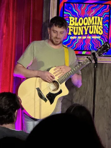 A performer playing an acoustic guitar on the Bloomin Funyuns stage
