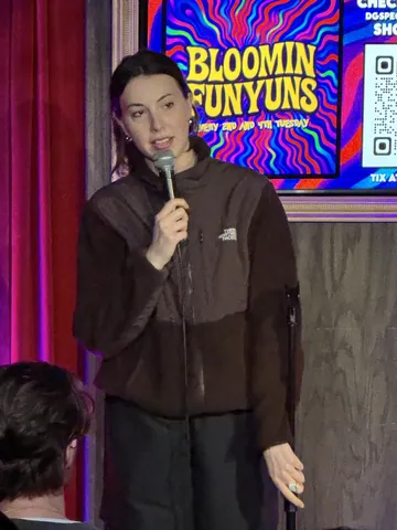 A comedian in a brown hoodie speaking into a microphone