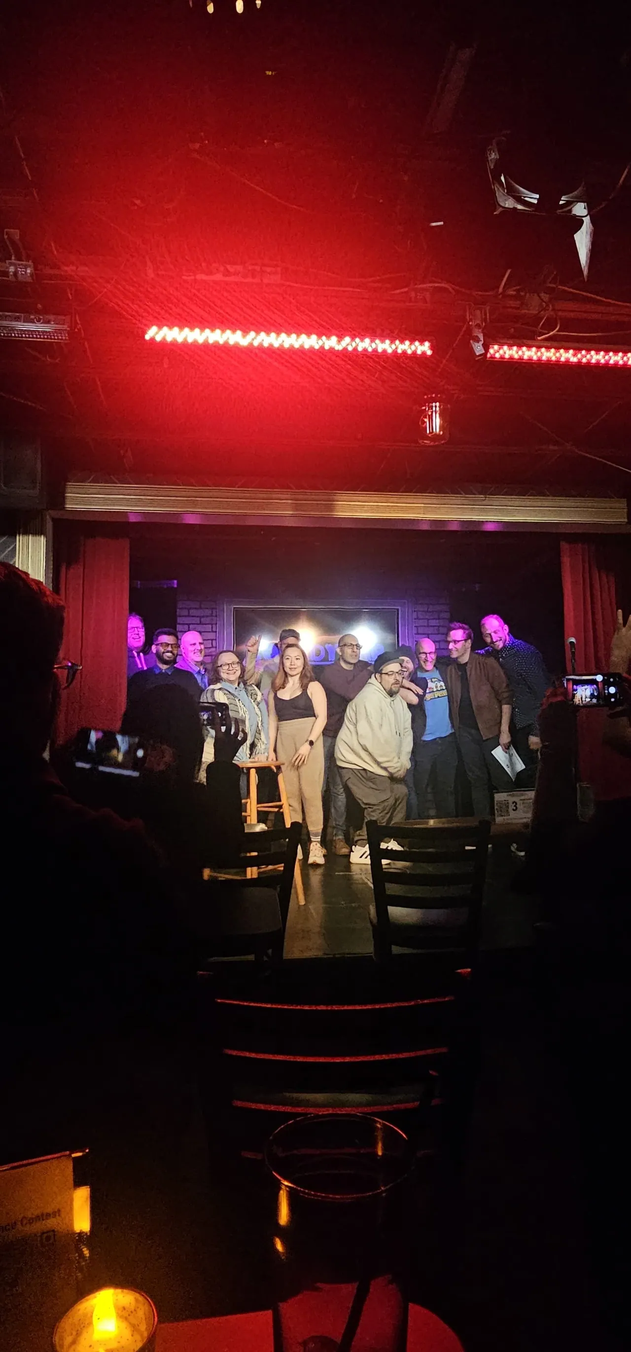 A group on a comedy stage photographed from the audience under red lights