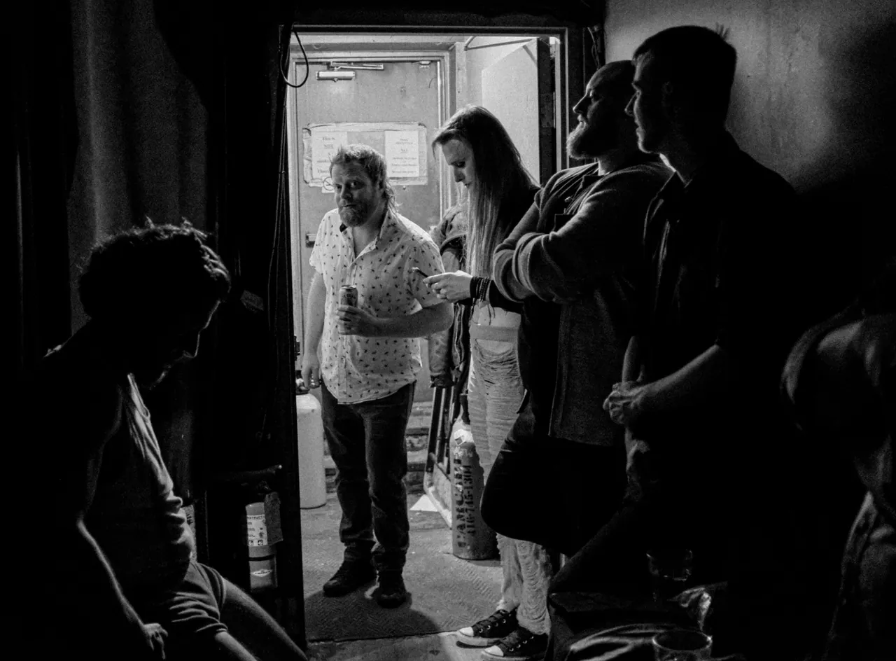 A black-and-white photograph of performers waiting together beside a backstage doorway