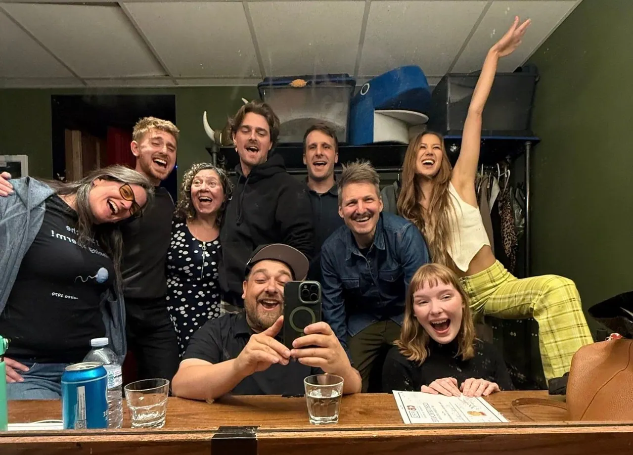 A group laughing together in a backstage mirror, with one person raising an arm in celebration