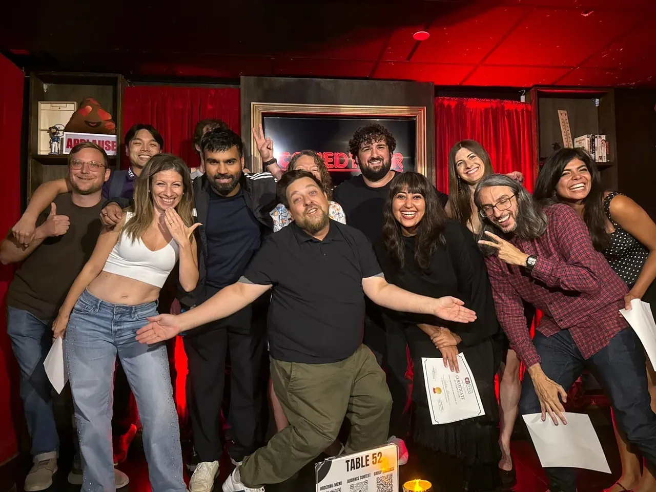 A group celebrating on the Comedy Bar stage, with completion certificates and big smiles