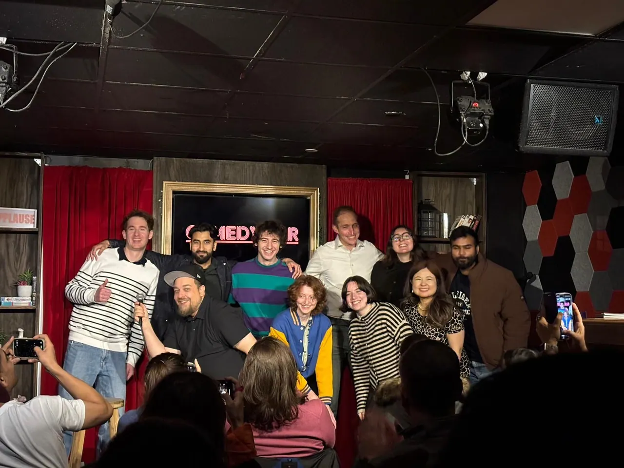 A group posing on stage as audience members photograph them