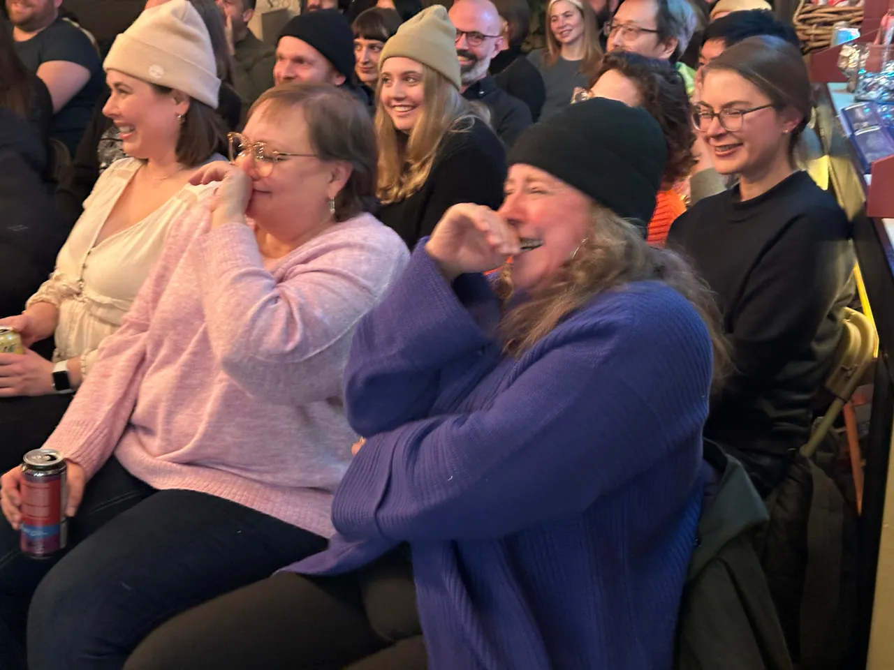 Audience members in lavender and blue sweaters laughing together in the front row
