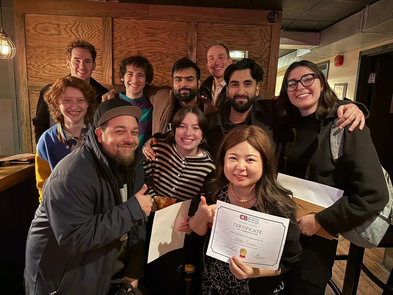 A smiling group in a wood-panelled lobby with completion certificates
