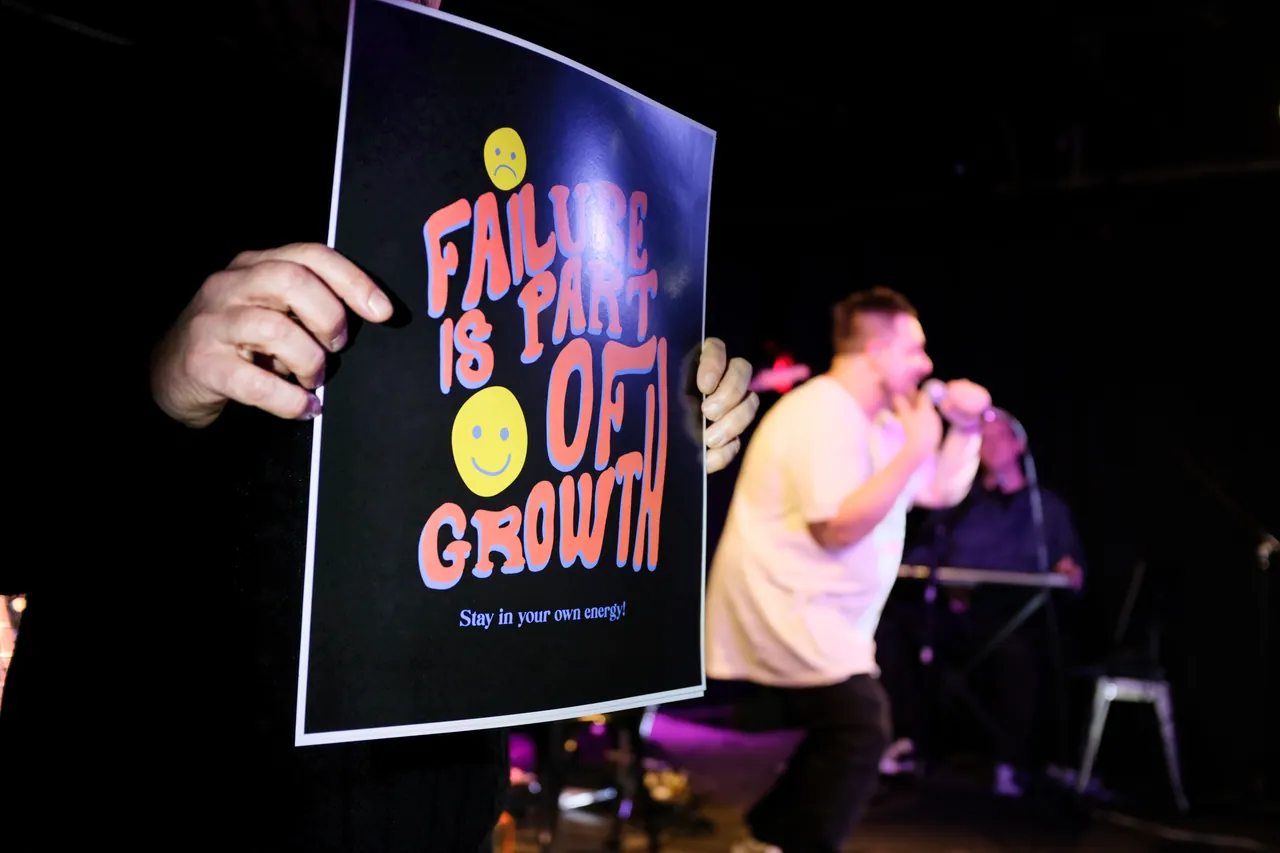 A sign reading Failure is part of growth with a performer singing in the background