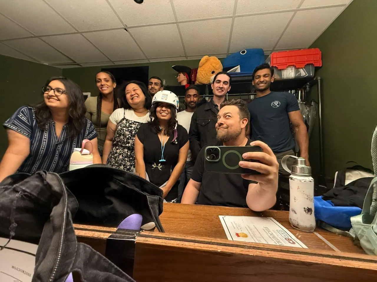 A group gathered in a green room with a bicycle helmet and props on a shelf