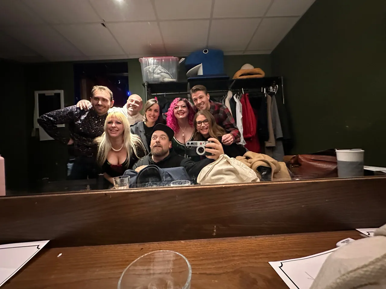 Seven friends smiling together in a backstage mirror