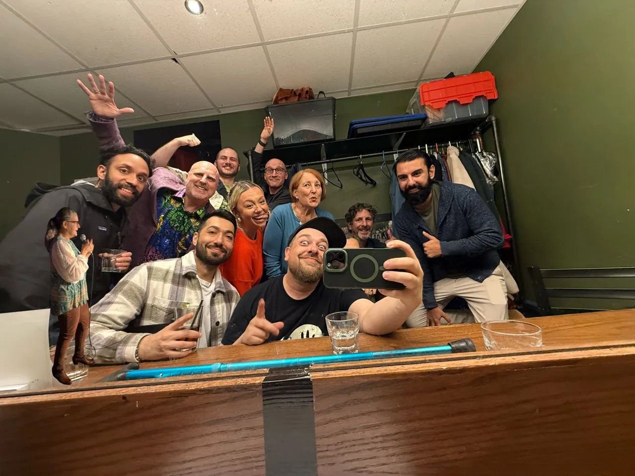 A playful backstage group photo with a small performer cutout added at the left