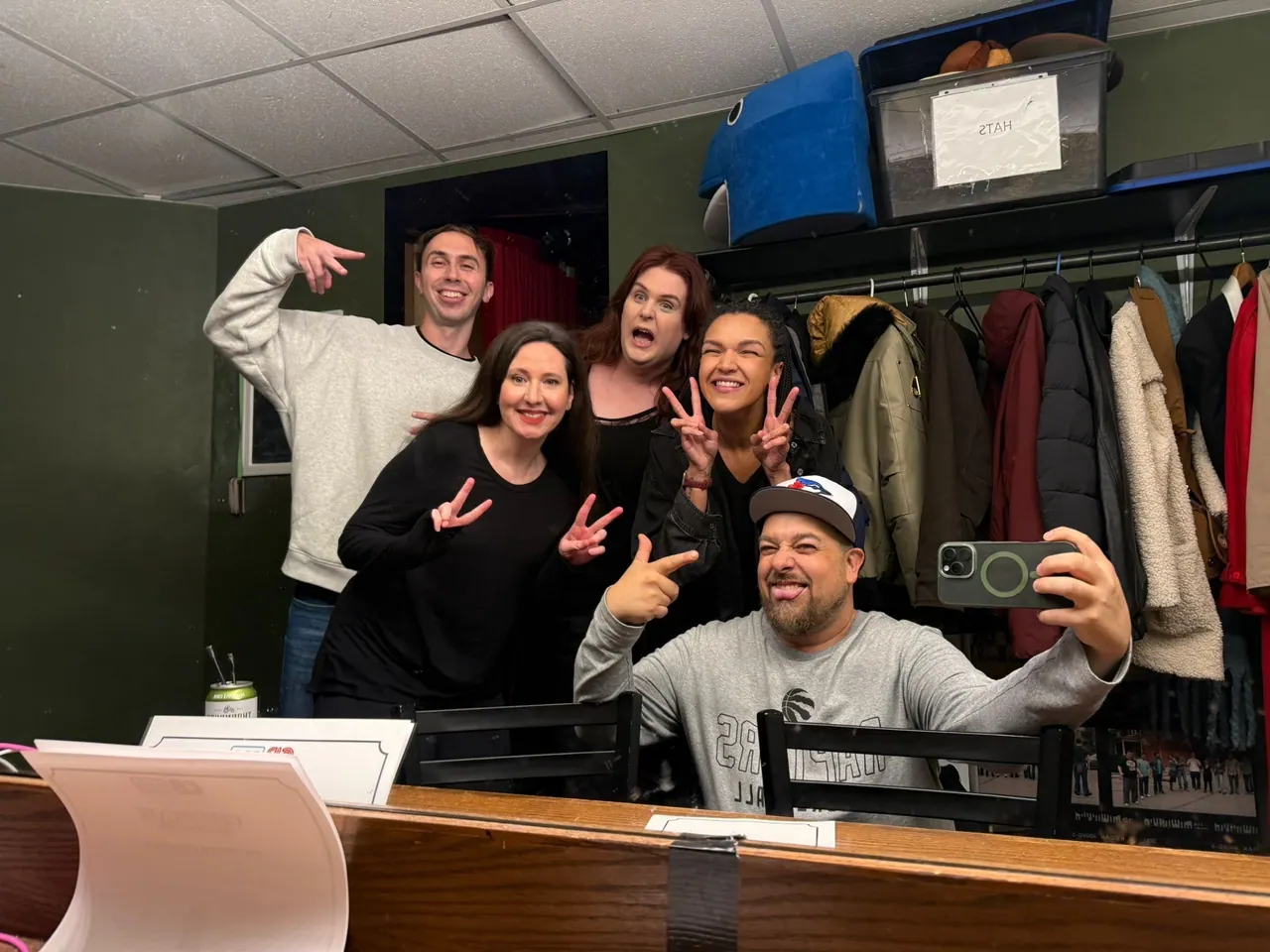 Five friends smiling and making peace signs in a backstage mirror