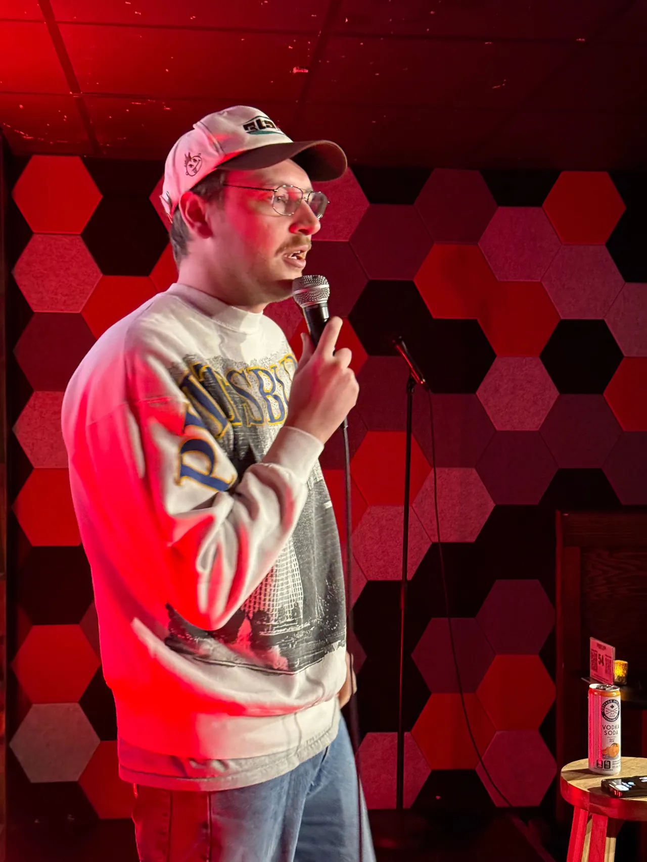 A performer in a cap holding a microphone in front of red and black acoustic panels