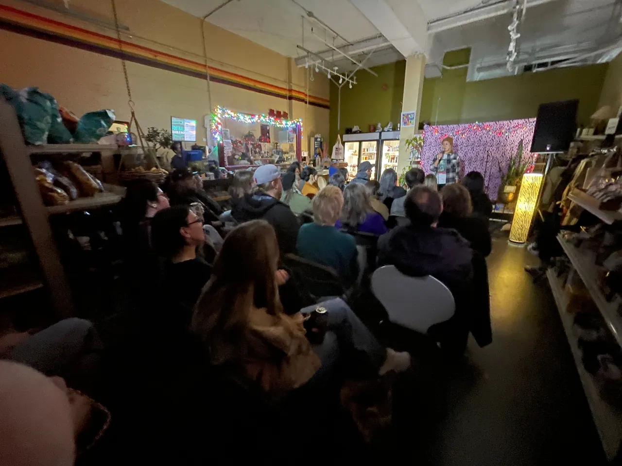 An audience watching a performer between the shelves of a neighbourhood shop