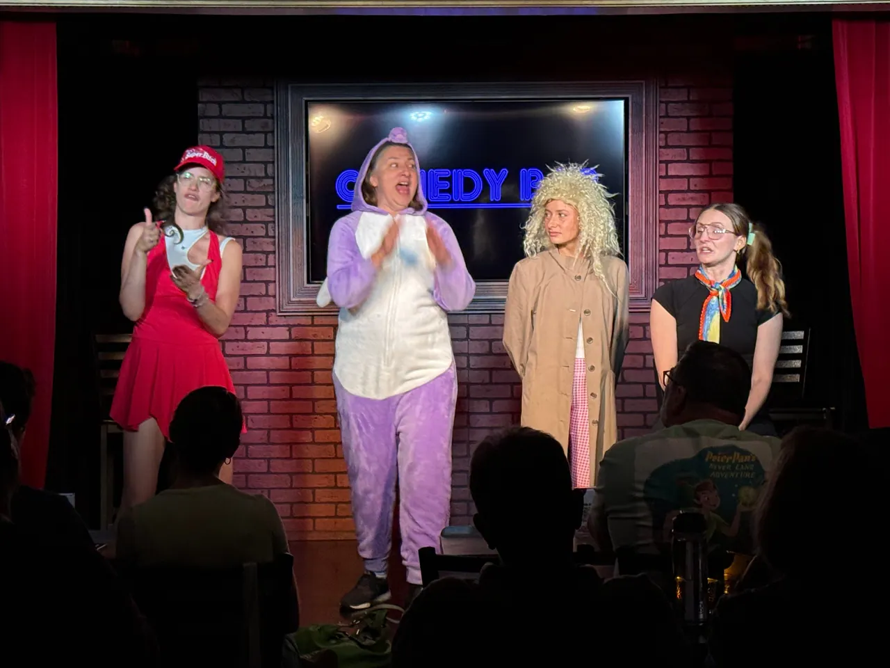 Four performers on the Comedy Bar stage, with one speaking into a microphone
