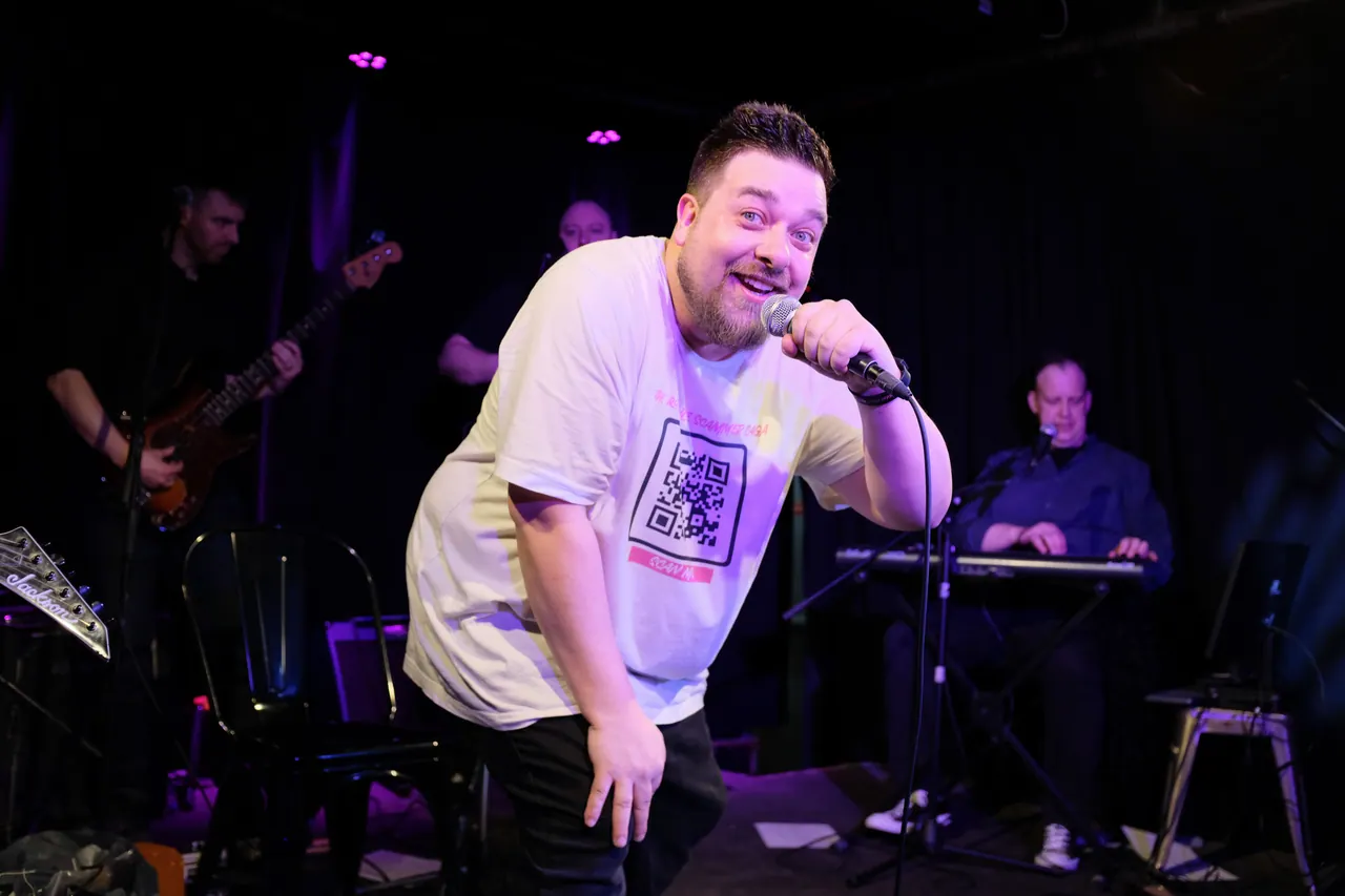 A performer leaning towards the audience with a microphone, with a live band behind him
