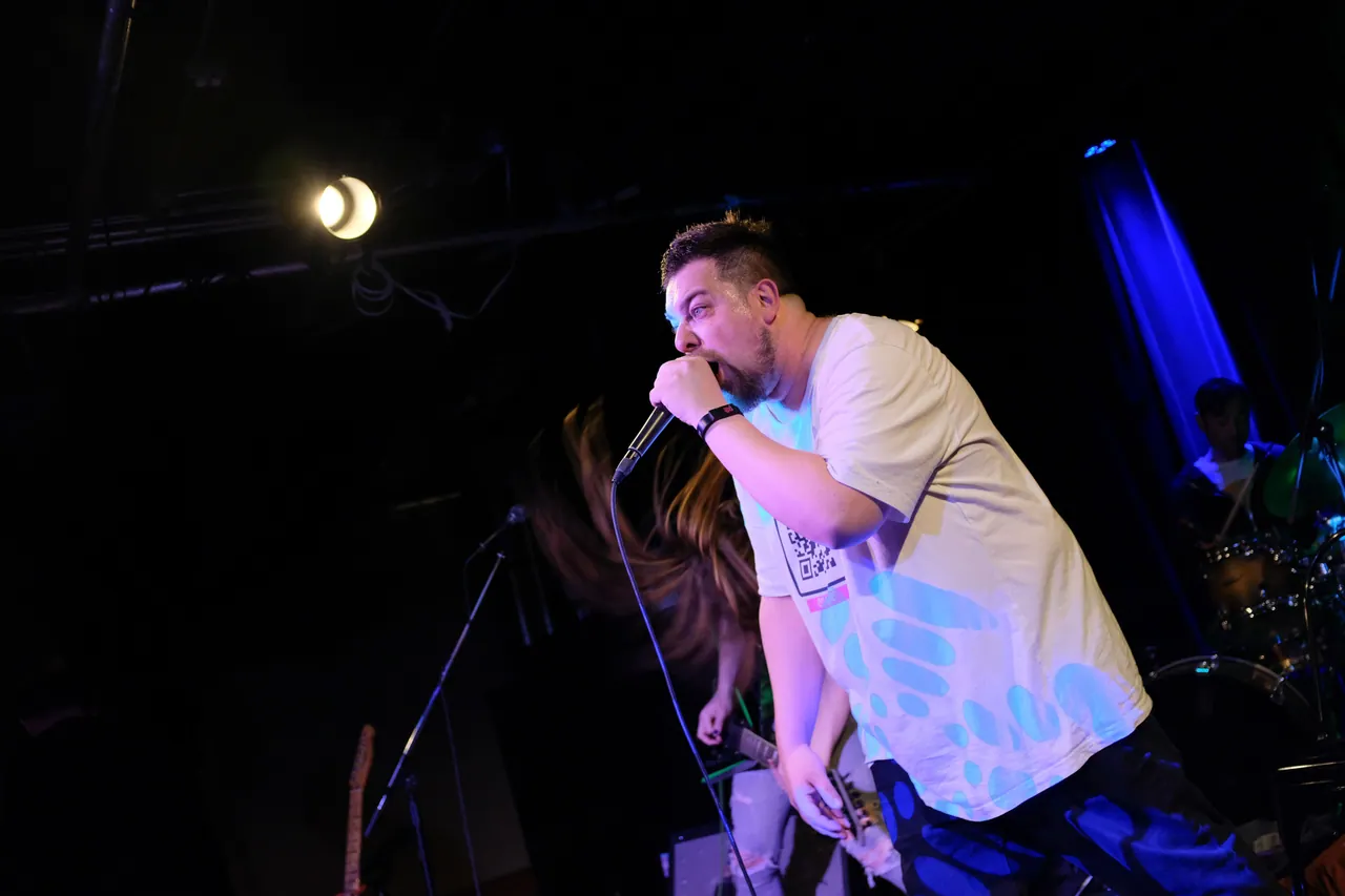 A performer singing into a microphone under blue and purple stage lights