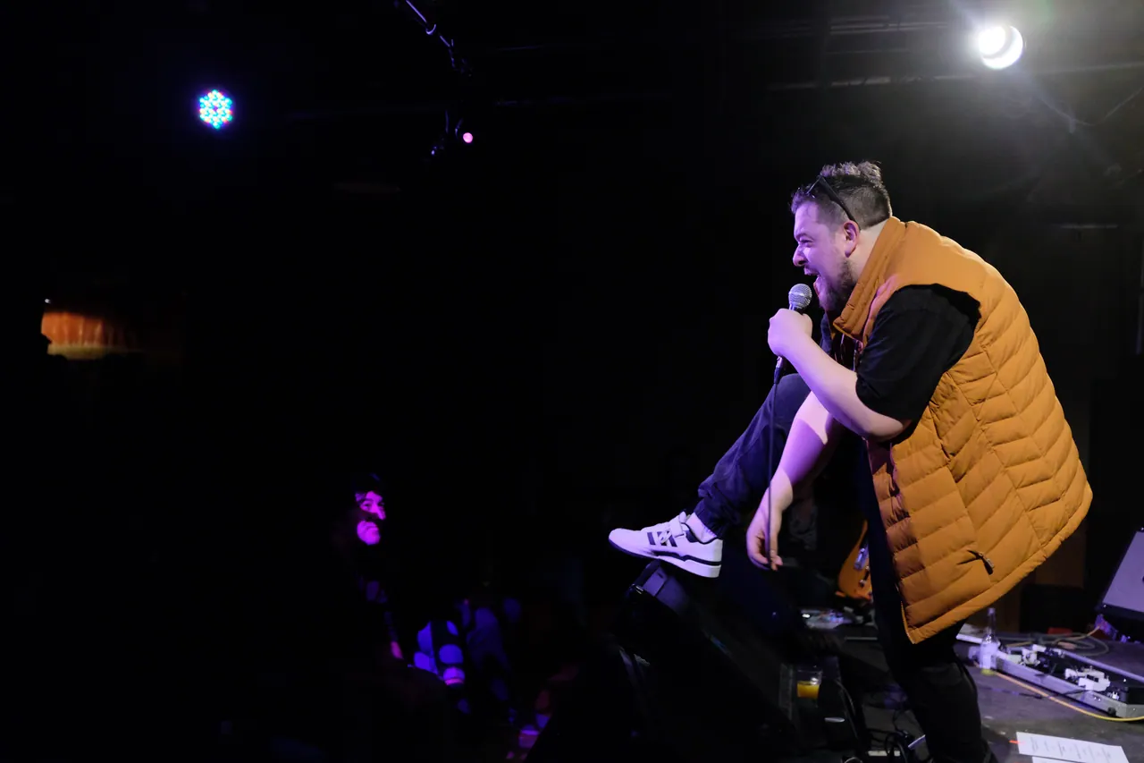 A performer in a yellow vest leaning towards the audience with a microphone